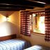 Pouso Sambaquis in Ilhabela: twin beds in a rustic guest room with wood beams and checkered curtains