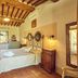 Agriturismo Palazzi del Papa in Pienza bedroom with rustic wood beams, wrought-iron bed, and window view