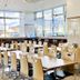 Toyoko Inn Higashi hiroshima Ekimae dining area with long tables, chairs, and large windows in Higashihiroshima