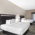 Best Western Plus McDonough Inn & Suites guest room with two beds, wall-mounted TV, and window with sheer curtains