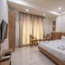 Hotel G Shy, Bhopal guest room with king bed, TV, and chairs by curtained window