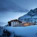 Hotel Zurserhof in Zürs at dusk, with a snow-covered mountain backdrop and illuminated windows