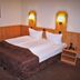 Hotel Frederikspark in Norderstedt: a double bed with wall lamps, nightstand and wood-paneled headboard.