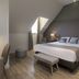 Aux Vieux Remparts in Provins: attic-style hotel room with king bed, desk, chair, bench and skylight