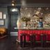 Hotel Saint Vincent in New Orleans bar with red front, dark stools, floral wallpaper, and bartender