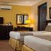 Herald Suites Solana Makati guest room with two beds, TV, dresser, mirror, and warm lighting
