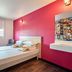 hotelF1 Annemasse room with double bed, bright pink wall, desk, chair and wall shelves in Saint-Cergues
