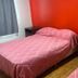 Hosteria Ailen in Ushuaia room with two pink-covered beds, bedside tables and red accent wall