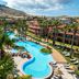 Pestana Porto Santo in Porto Santo with a winding outdoor pool, palm trees, and mountain backdrop.