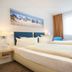 Hotel Nordraum Bremen guest room with twin beds, blue chairs, desk, and beach wall art