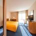 Apart-Hotel Halle in Halle: bright hotel room with yellow bed, desk, TV, and balcony doors