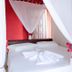 Pousada Mar de Araçatiba bedroom with white canopy bed, red accent wall, and folded towel