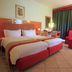 The Kairaba Beach Hotel in Serrekunda, guest room with twin beds, red seating, and large window drapes