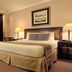 Herald Suites Solana Makati guest room with king bed, bedside lamps, armchair and framed wall art
