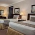 Herald Suites Solana Makati guest room with two beds, dresser, lamps, mirror, TV and air conditioner