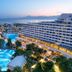 Titanic Deluxe Lara in Antalya with illuminated pools, palm trees and a sea view at dusk