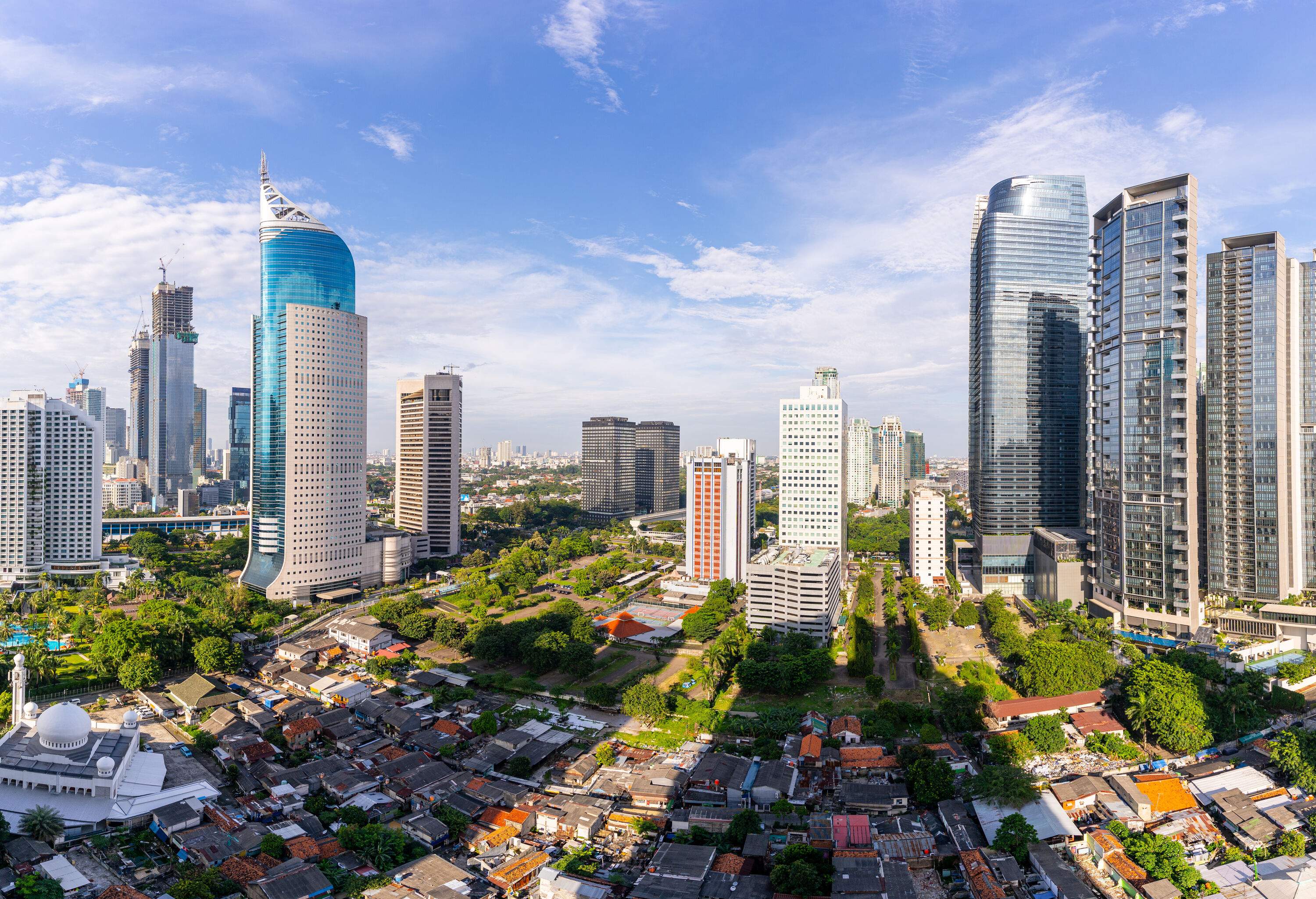 A white dome mosque dominates the compact cluster of tiny houses in the middle of glass skyscrapers.