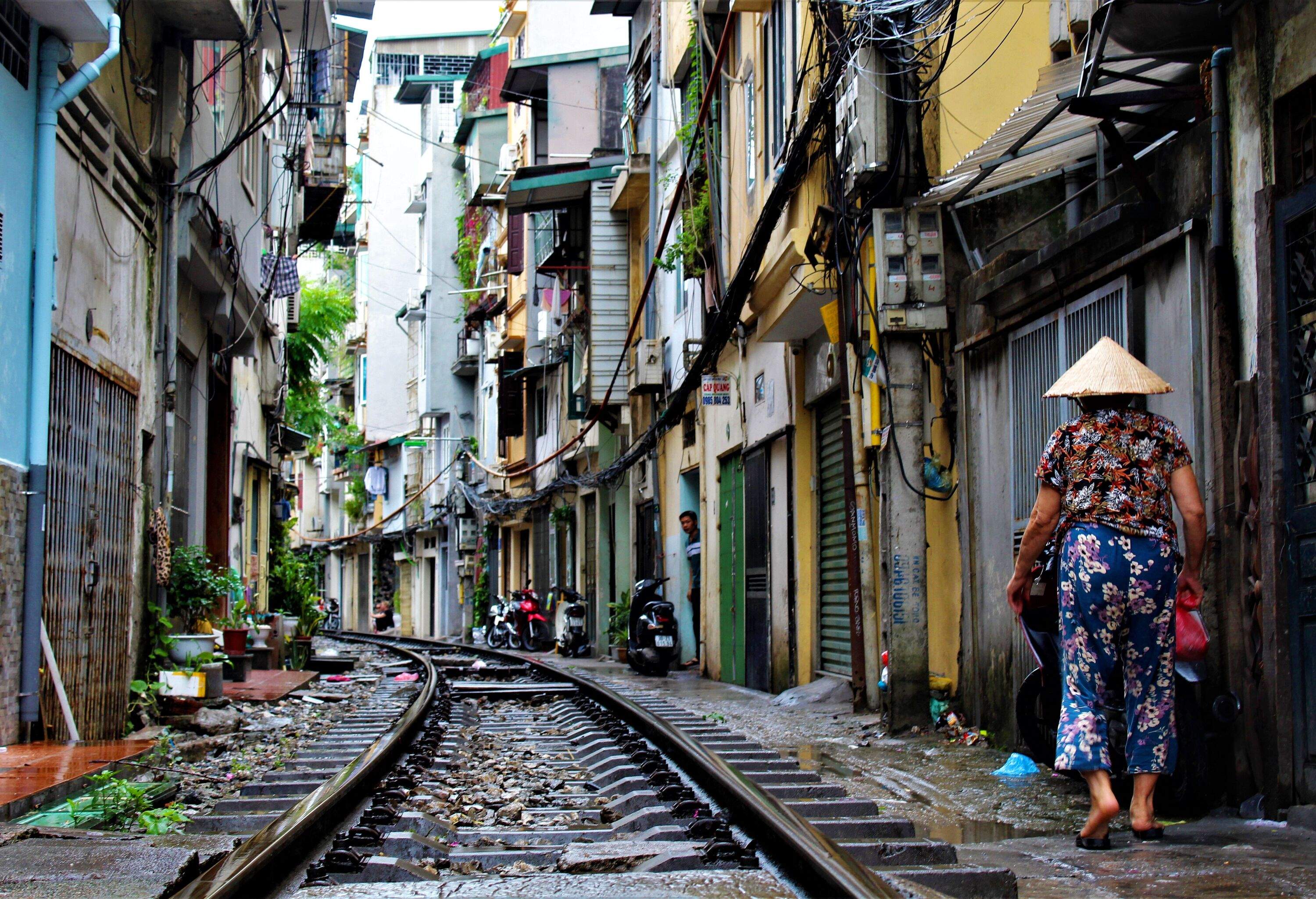 A person in a straw hat and colourful floral clothes strolls beside a railway in a residential neighbourhood.