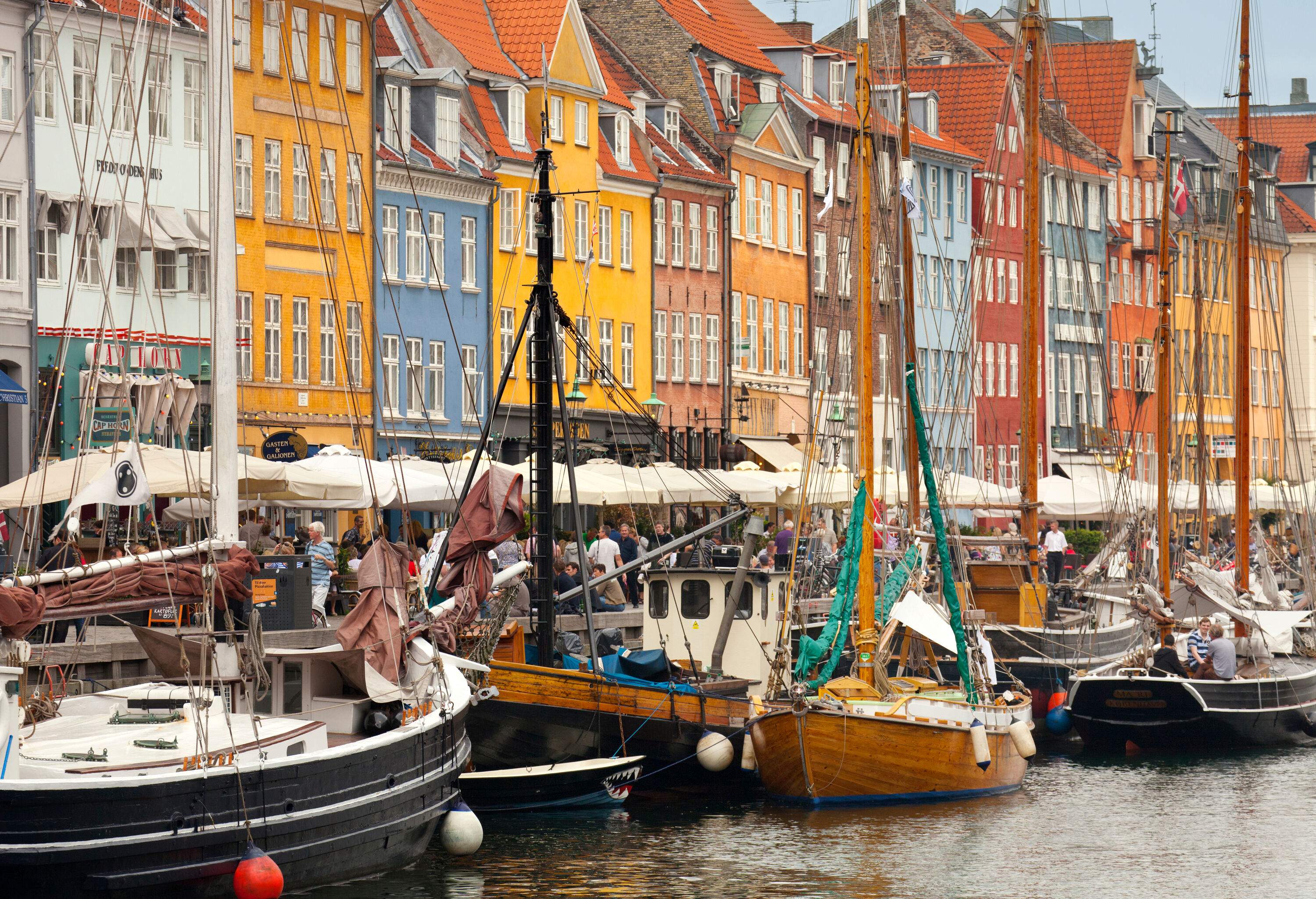 Harbour brimming with fishing vessels, with a promenade of shops and people on either side.