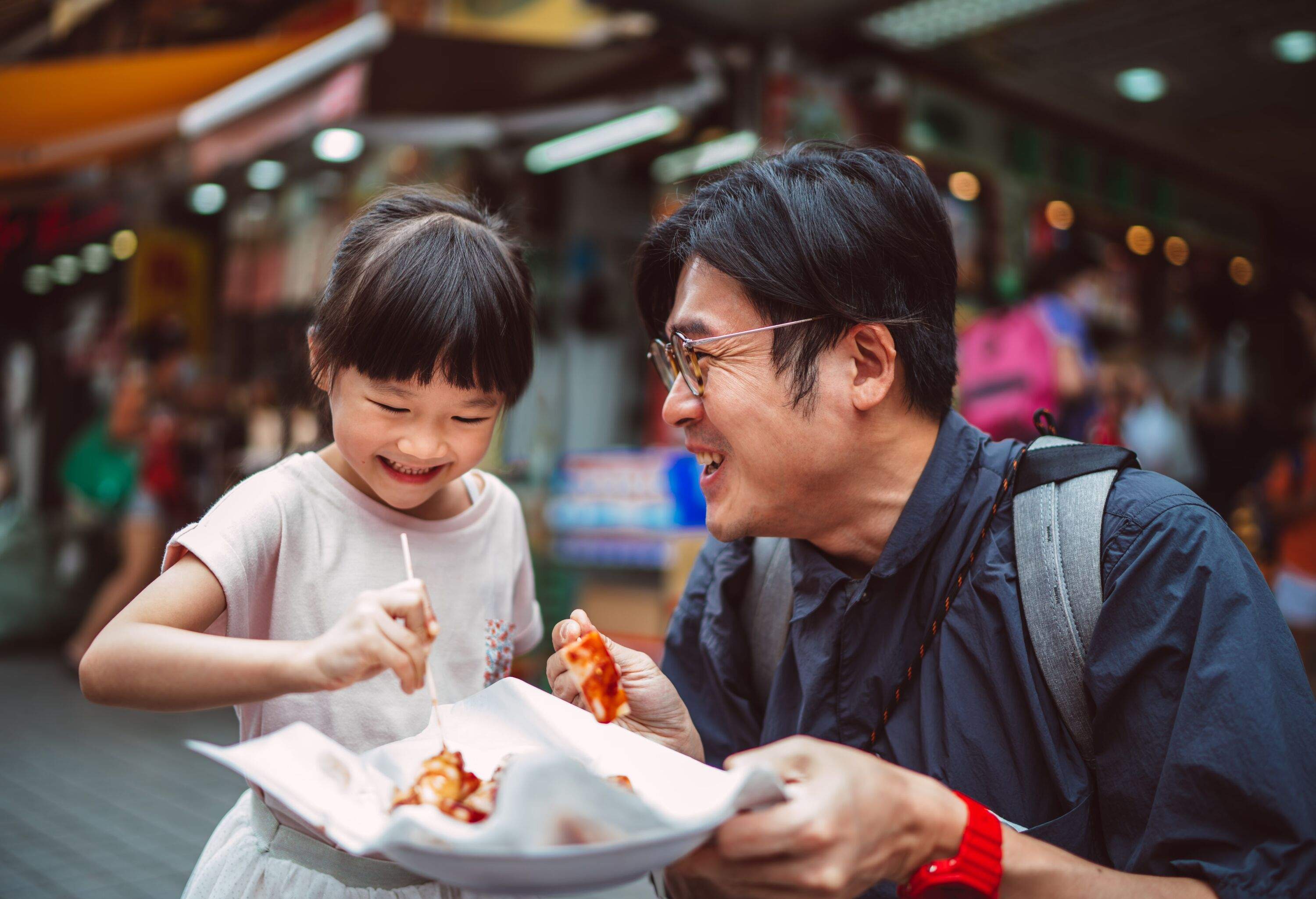 Lovely little girl enjoying Hong Kong local street food with her young handsome dad joyfully in street.