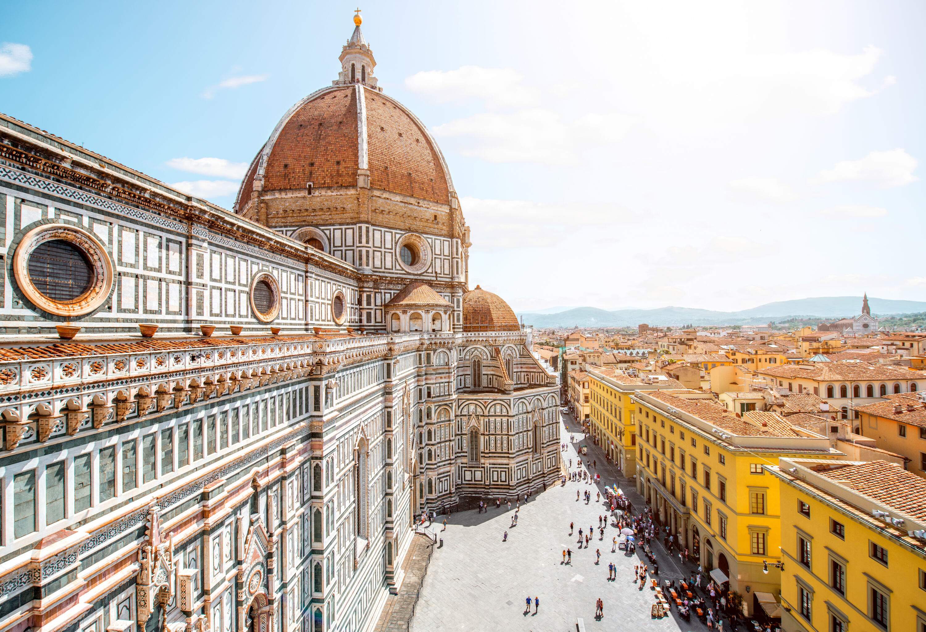 A stunning gothic-style cathedral with a red-tiled dome and an elegant, coloured marble facade in the centre of an old town.