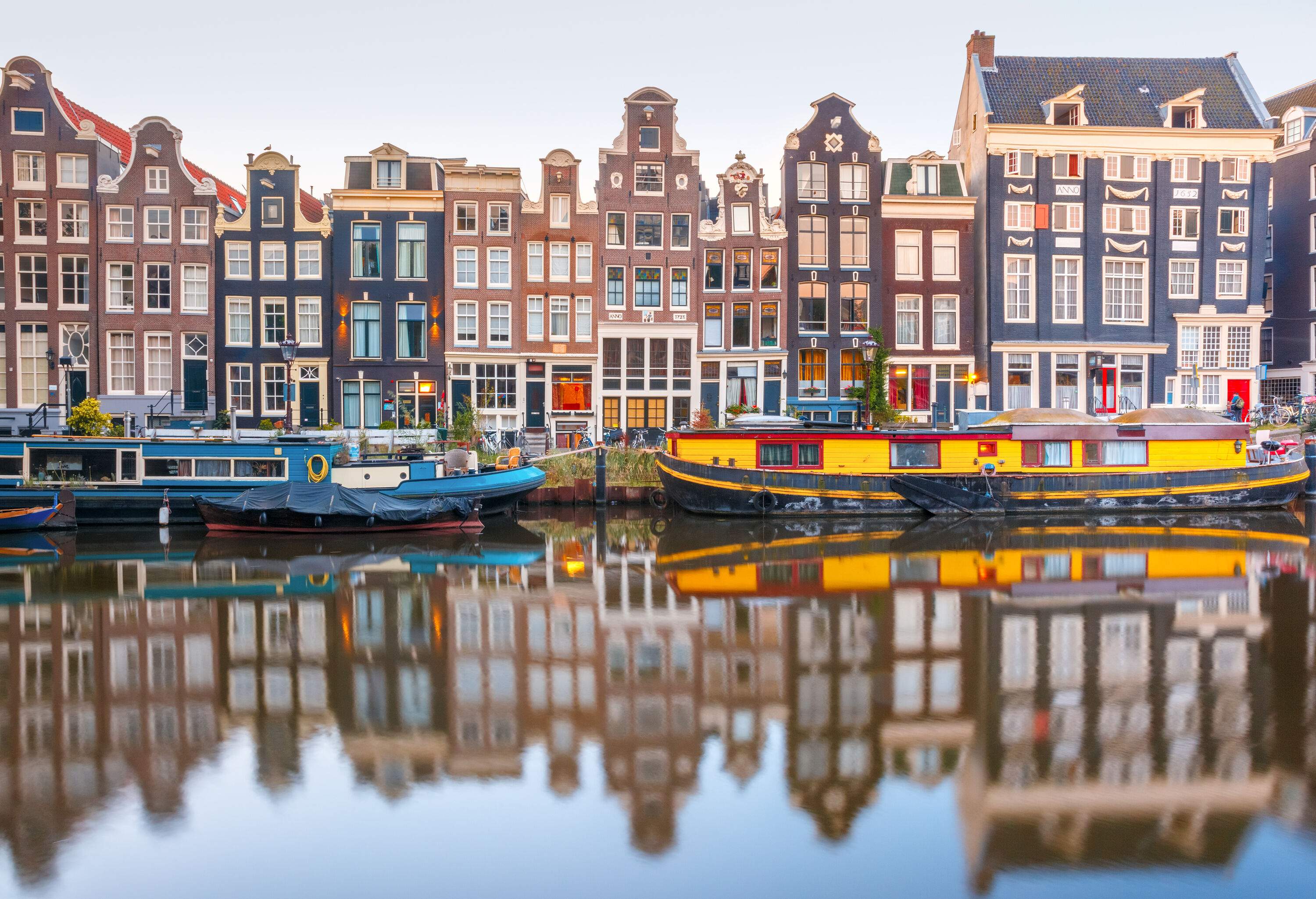 Blue and yellow houseboats moored on a canal in front of colourful narrow buildings.