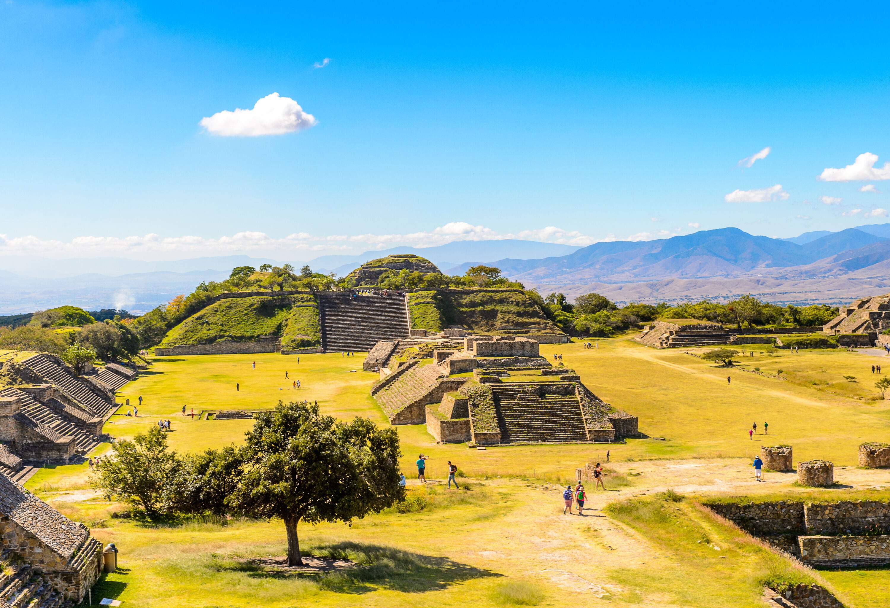 Tourists stroll across an archaeological site with ruins of Mayan pyramids.