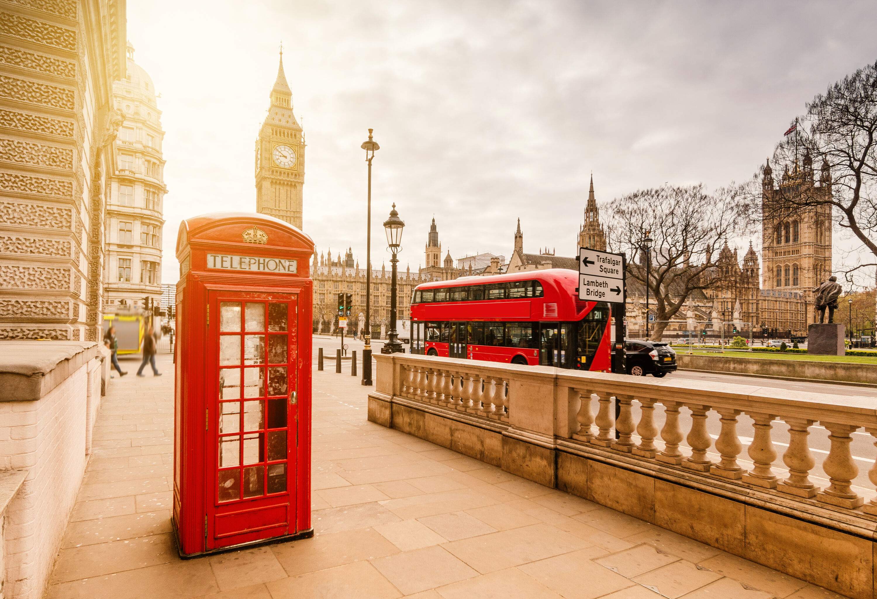 A classic red telephone booth, a red double-decker bus and Big Ben clock tower in the background against the cloudy sky.