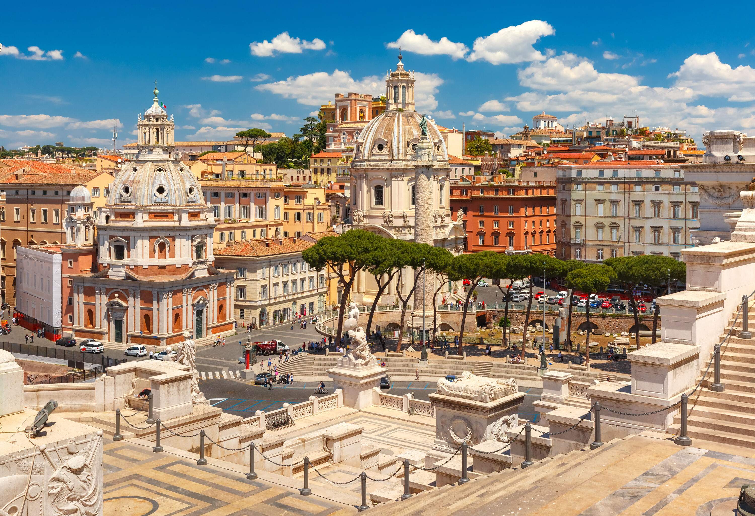 The Trajan's Column erects facing two gigantic dome churches surrounded by tall colourful buildings.