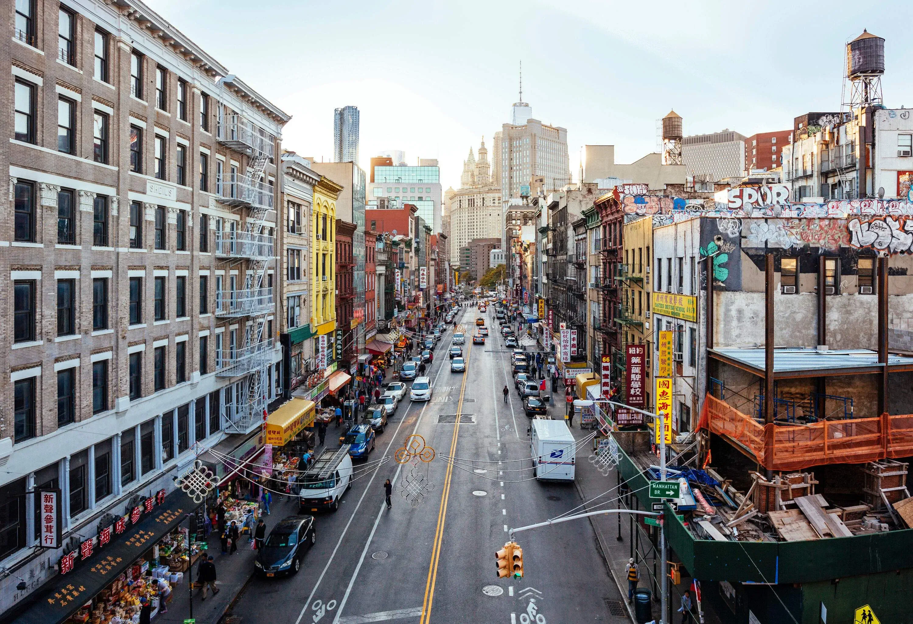 Cars travel on a road lined with parked cars and colourful adjacent apartment buildings.
