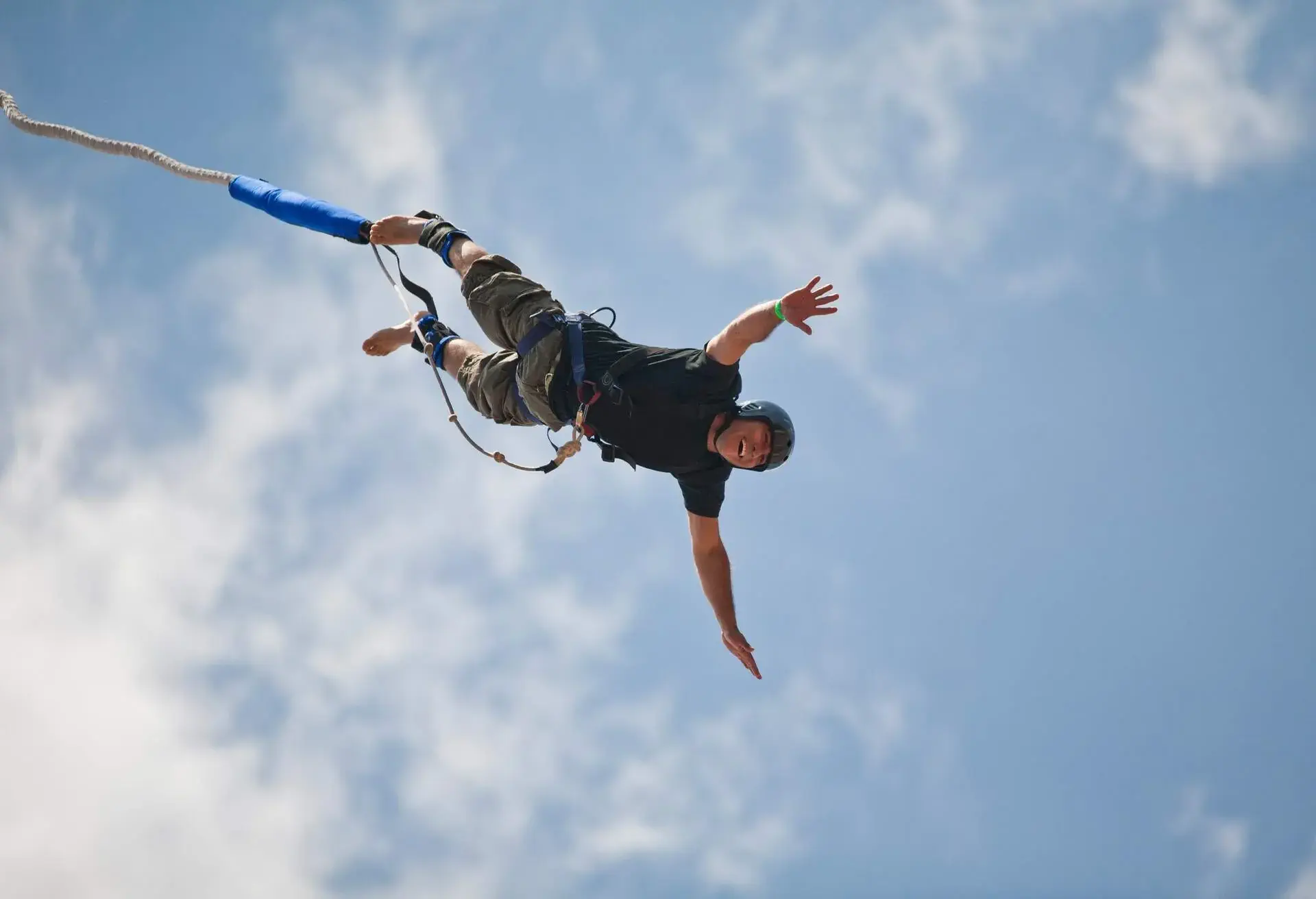A man in a helmet bungee jumps while attached to a rope.