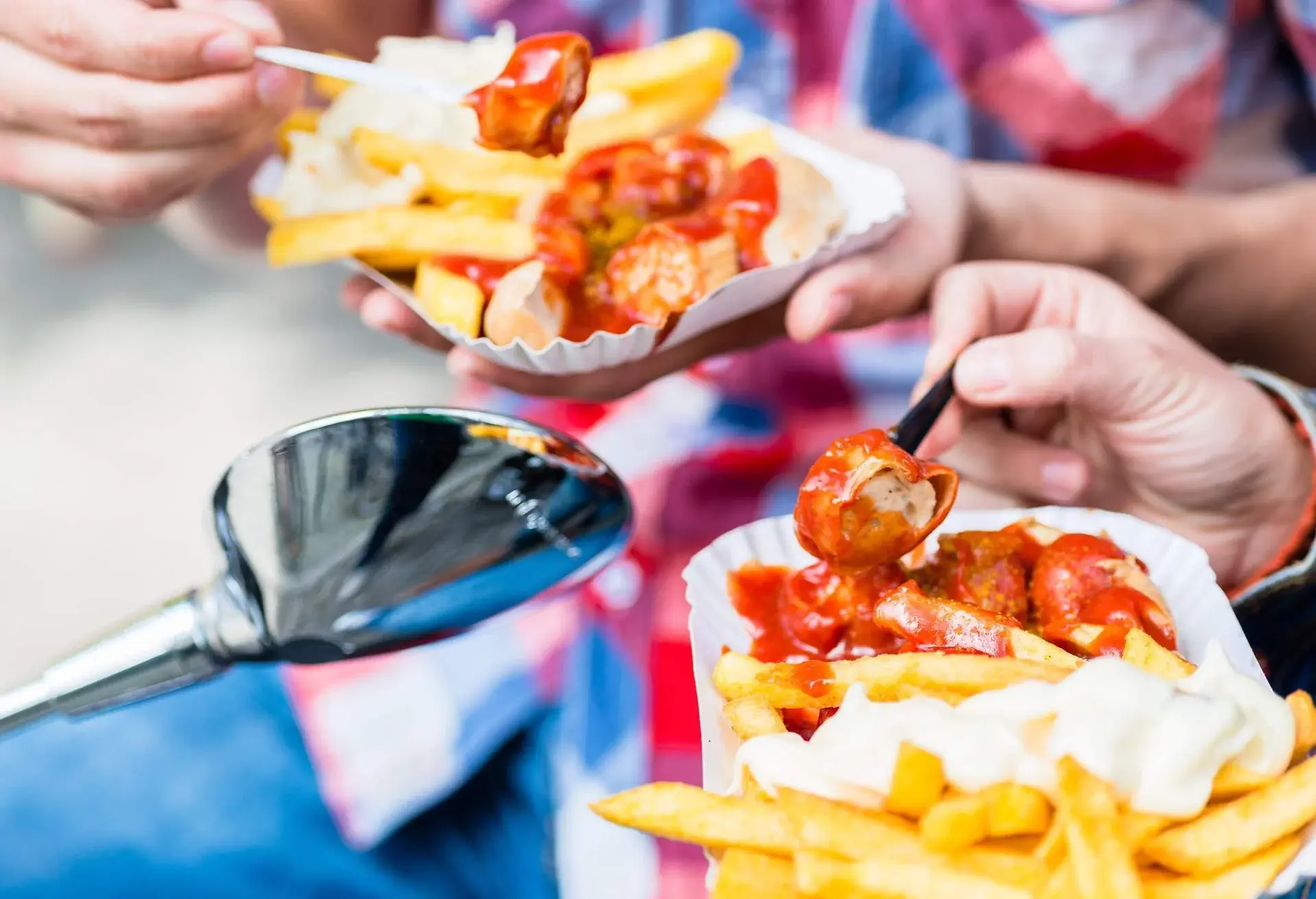 White paper plates with cut up currywurst and french fries with mayo