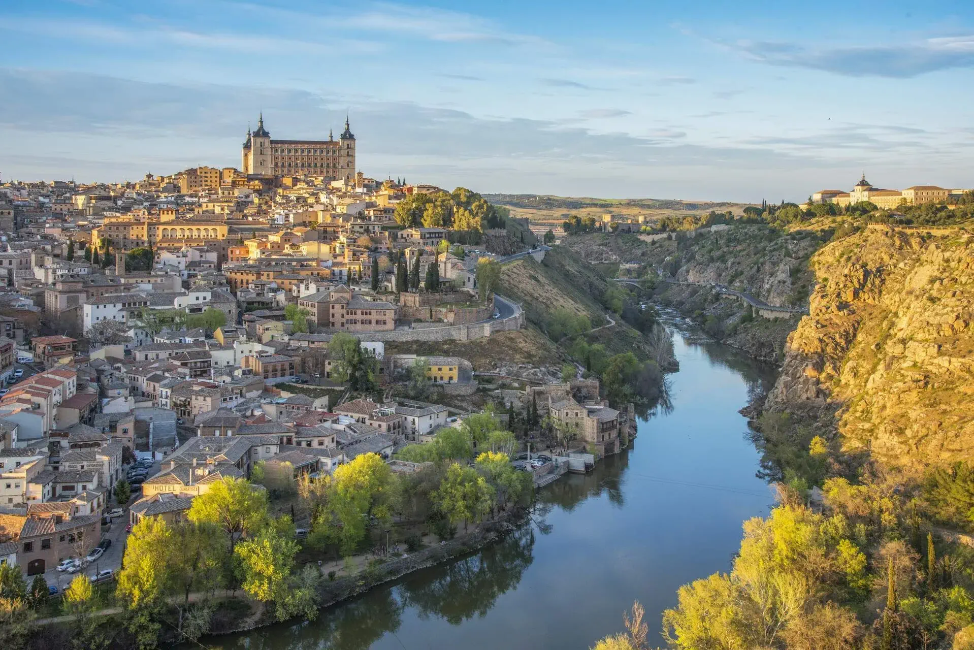 A calm river flows at the foot of a hill full of houses with a church lying on top.
