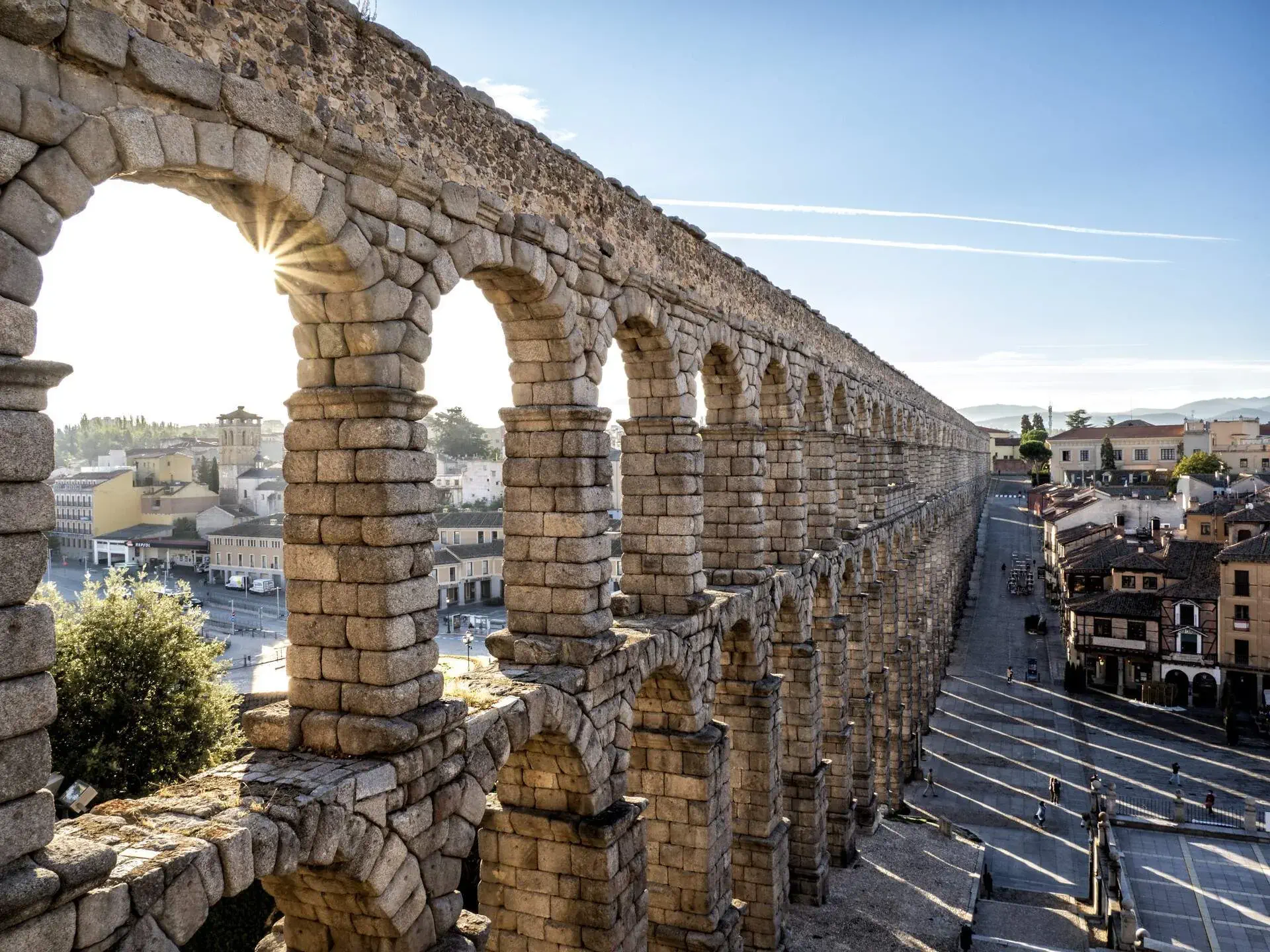 A two-storey stone arcade across a city street lined with houses and buildings.