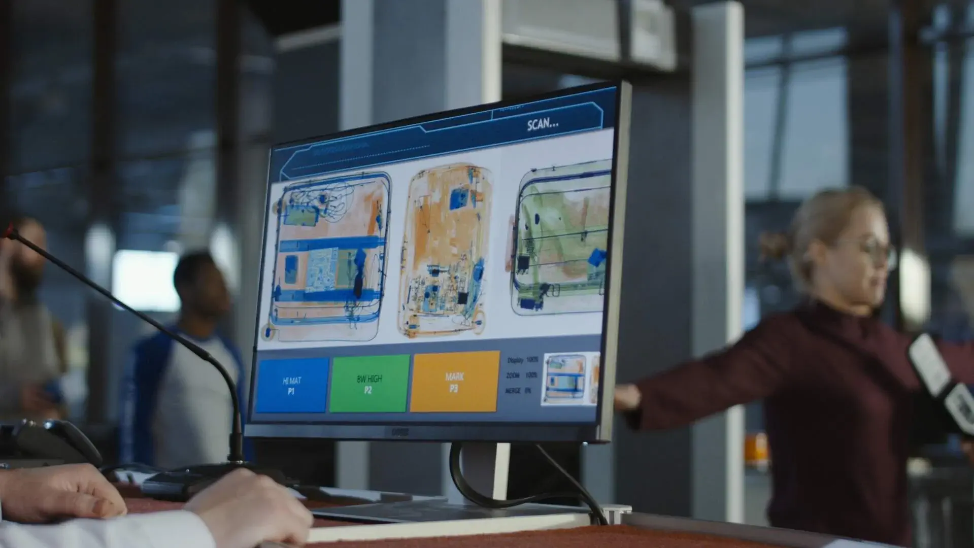 A screen in the airport security area showing whats inside a suitcase while we see a woman in the background being checked in the scanner
