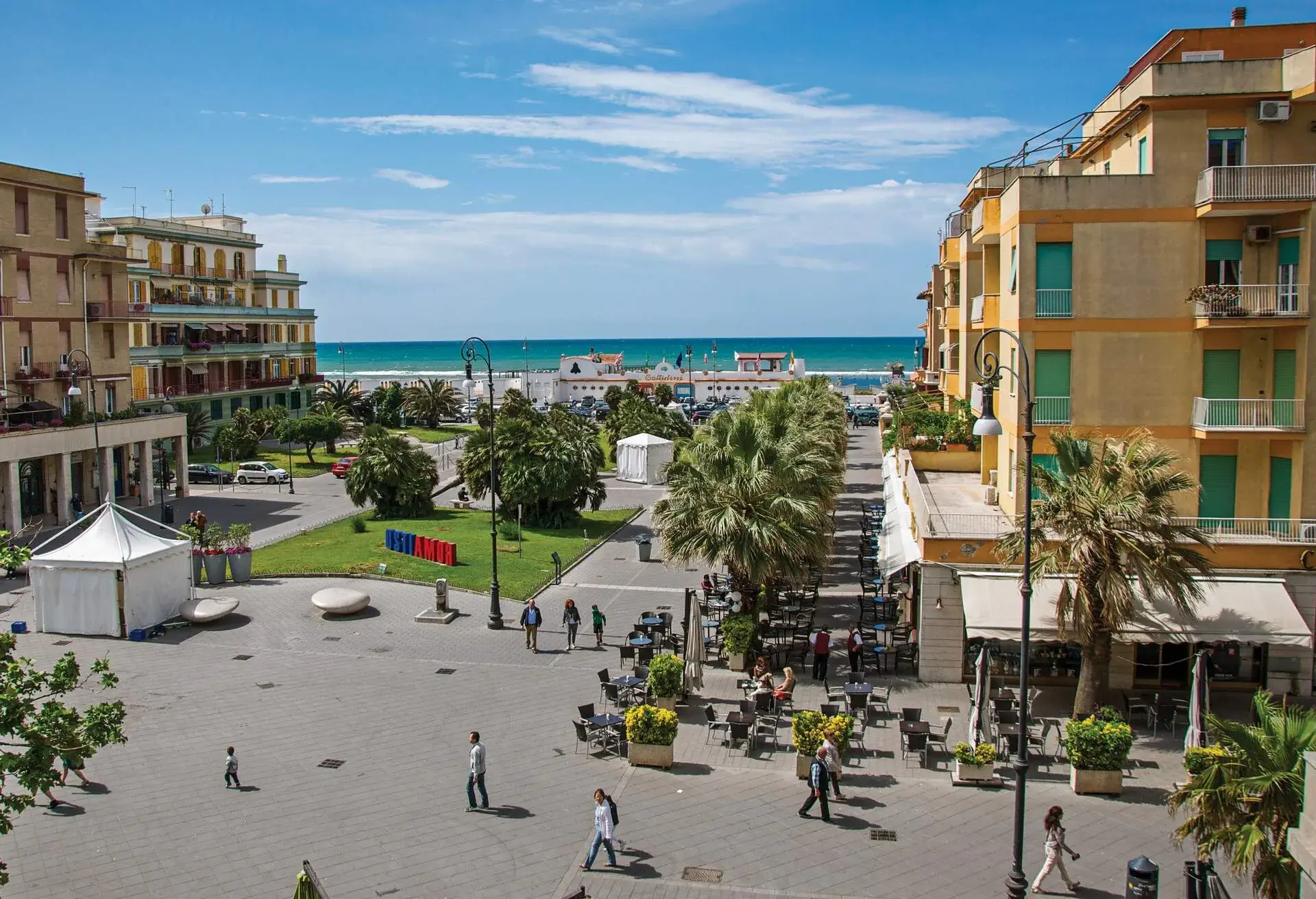 Aerial view of a coastal city with a plaza surrounded by buildings overlooking the tranquil blue sea.