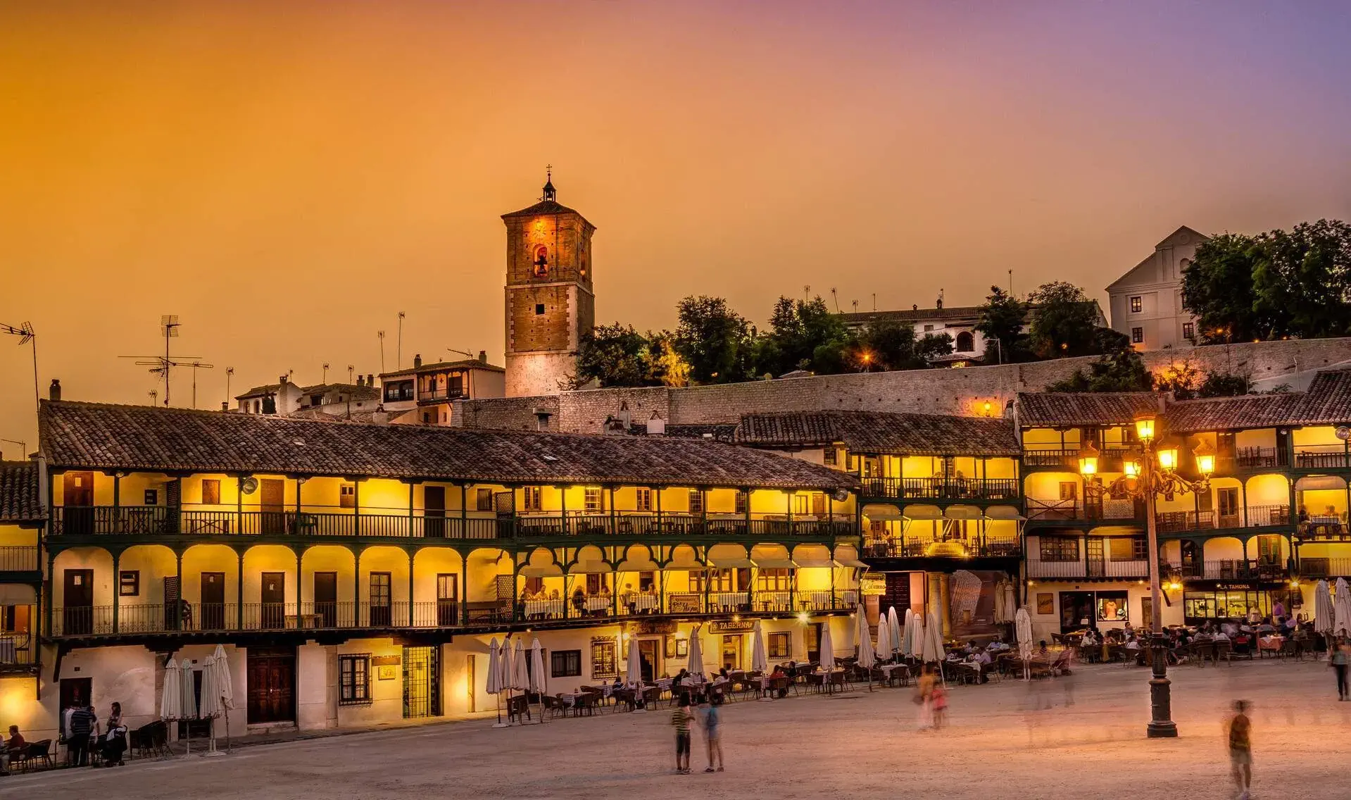 A public square surrounded by lit up buildings and outdoor dining establishments.
