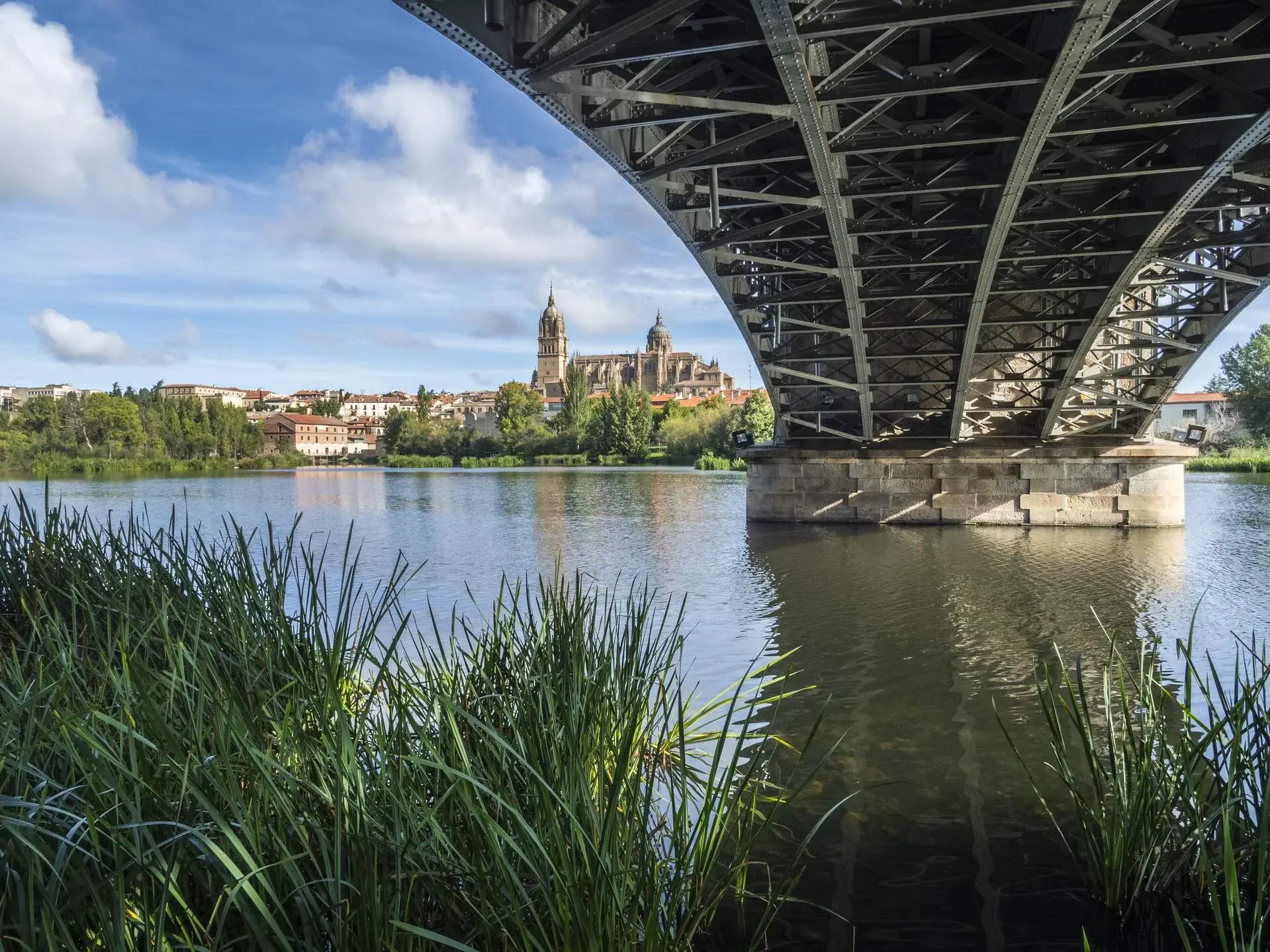 Side view of a cathedral viewed from the river with calm water running under the bridge.