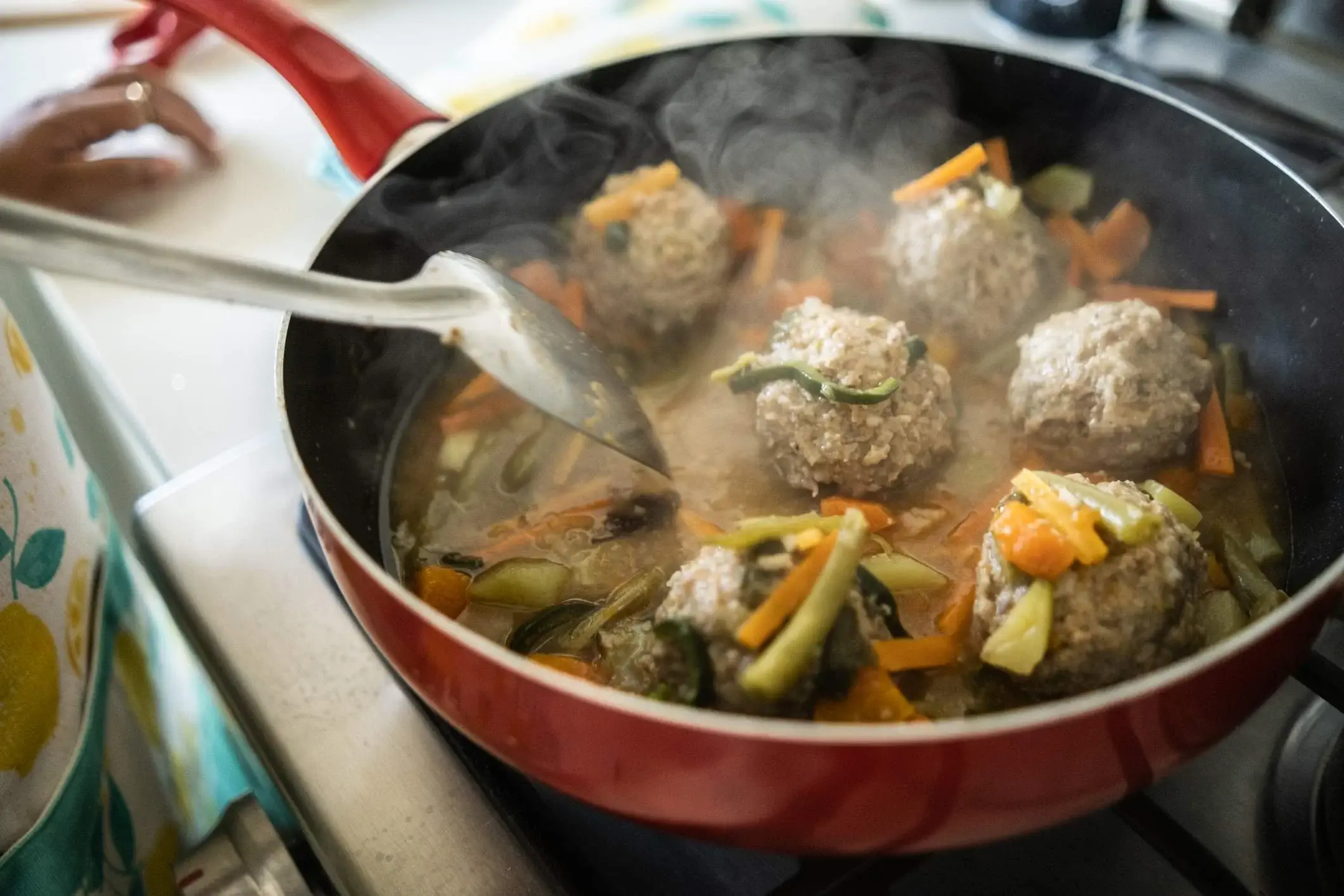 Albondigas being fried in a pan with veggies