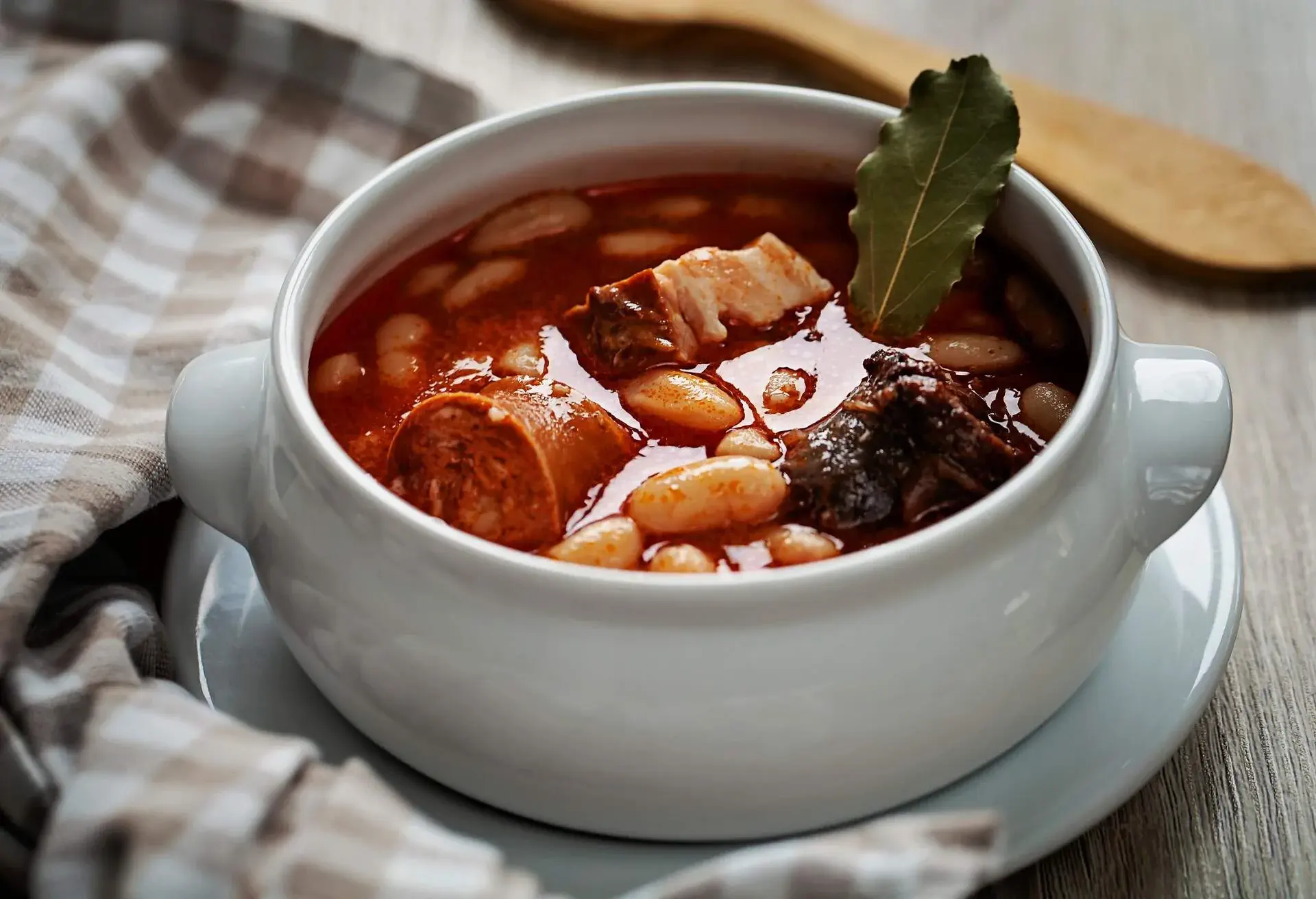 Fabada stew in a white bowl with a checkered napkin