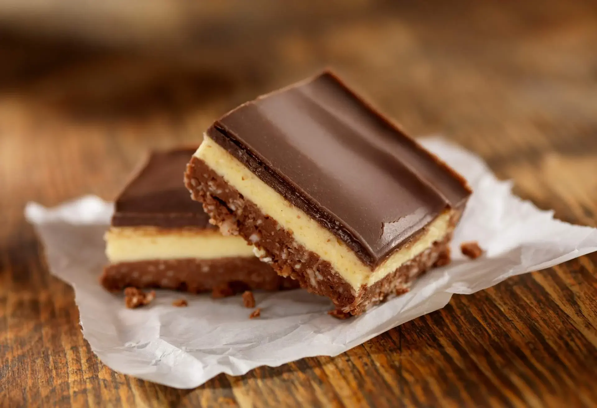 Two Nanaimo Bars on white paper and a wooden surface