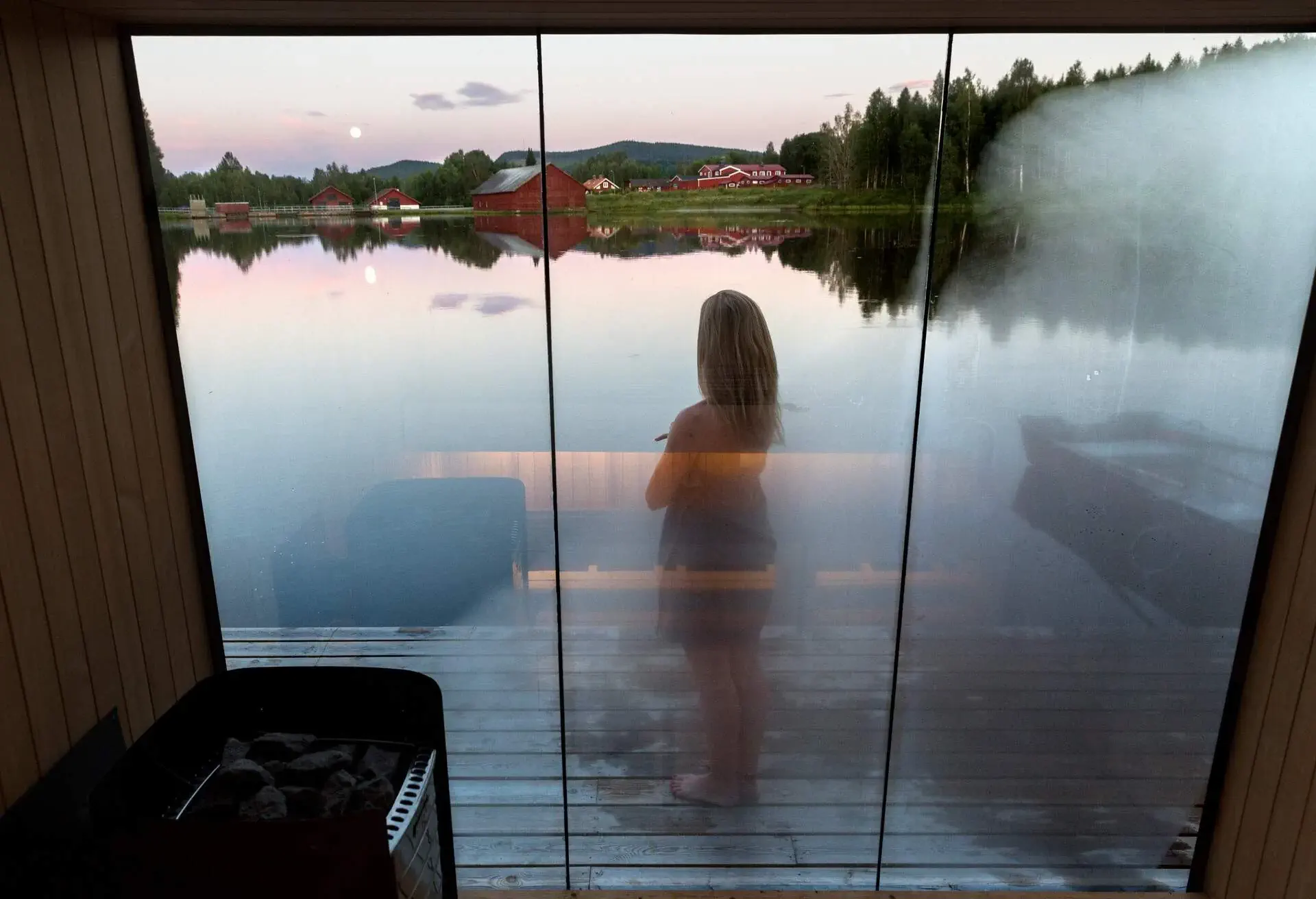 A photo of a woman outside a sauna boat on top of a lake.