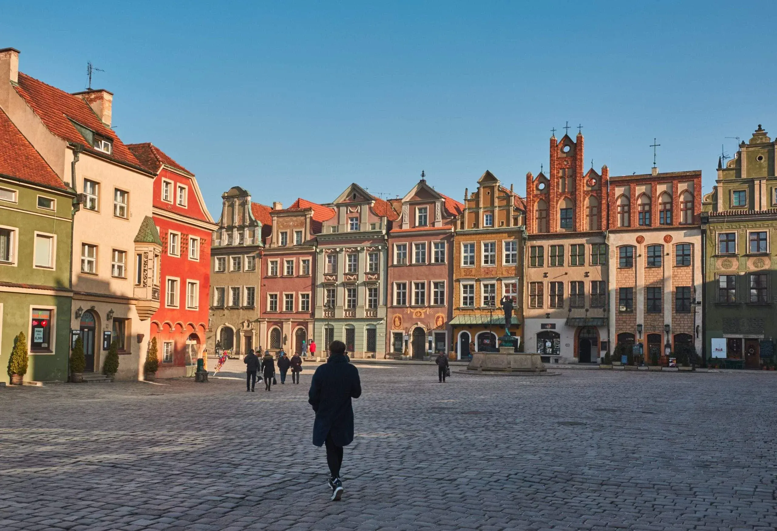 Pedestrians stroll across a cobblestone public square surrounded by adjacent city buildings.