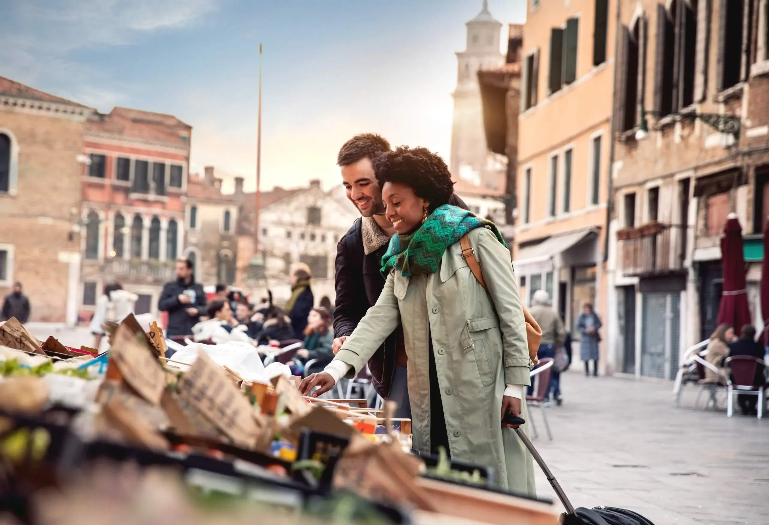A couple in trench coats browse a display of souvenirs on the streets.