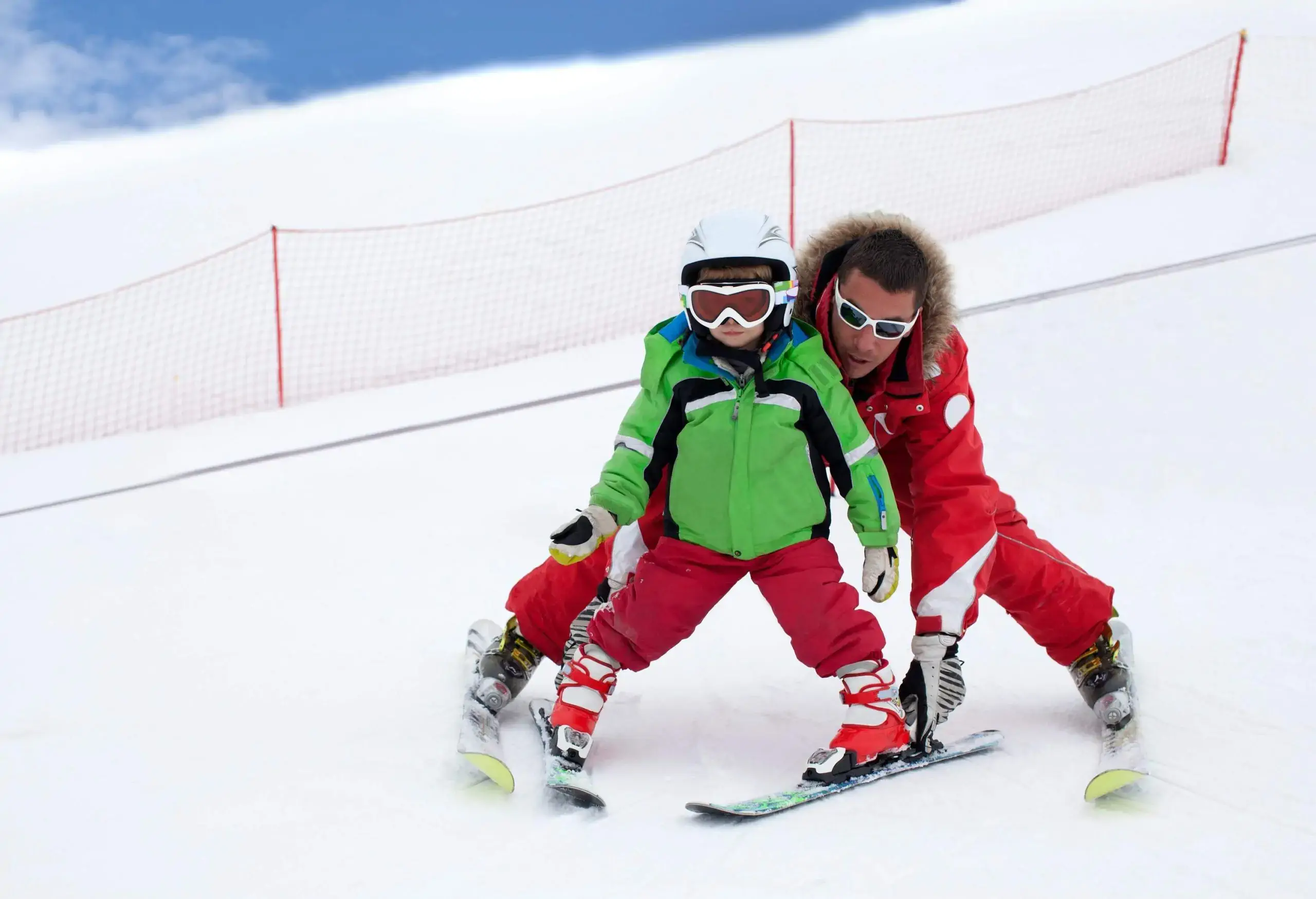 A man assisting a kid as they go down a ski run.