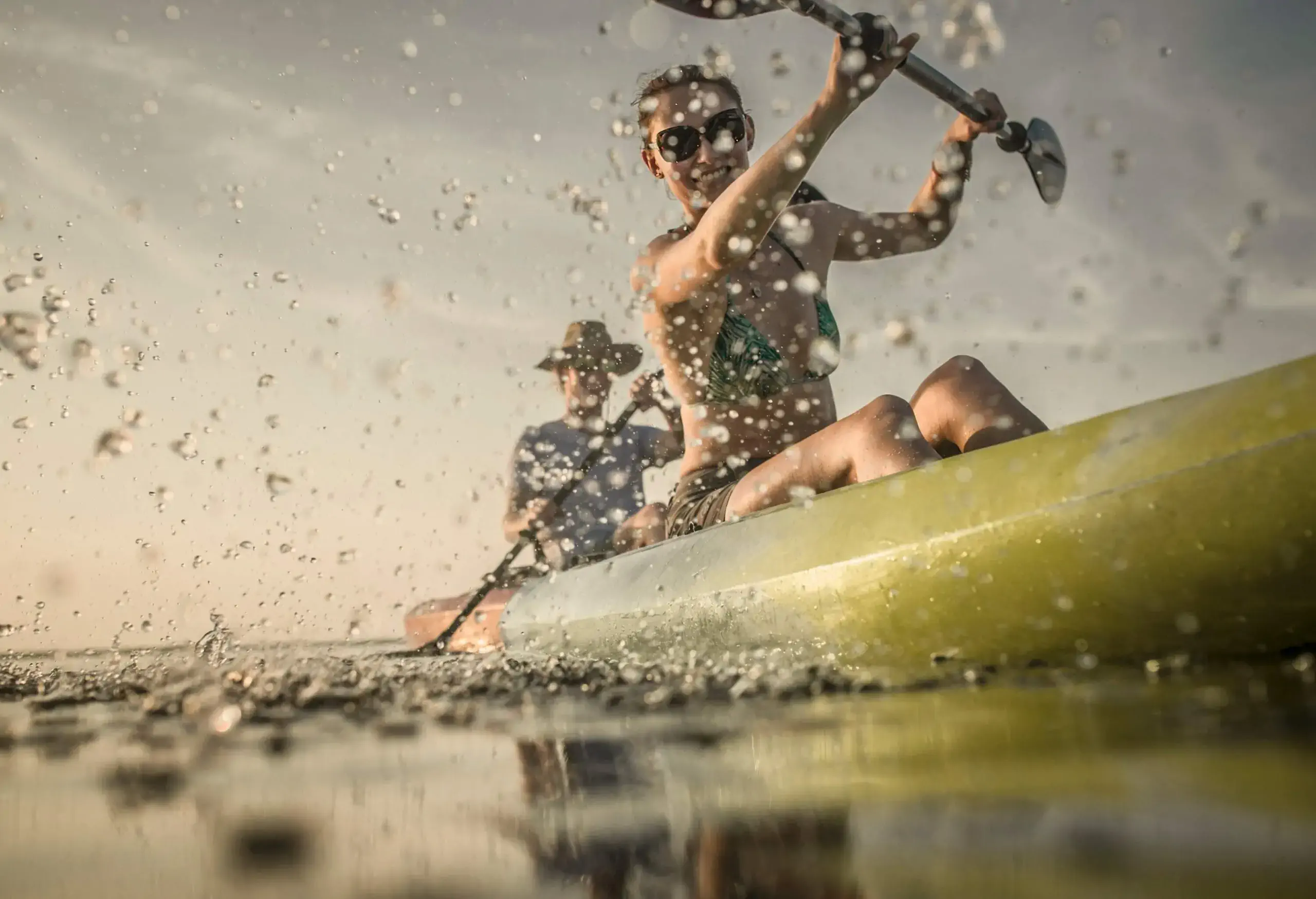 Two people on a canoe paddling across a lake, creating splashes of water.