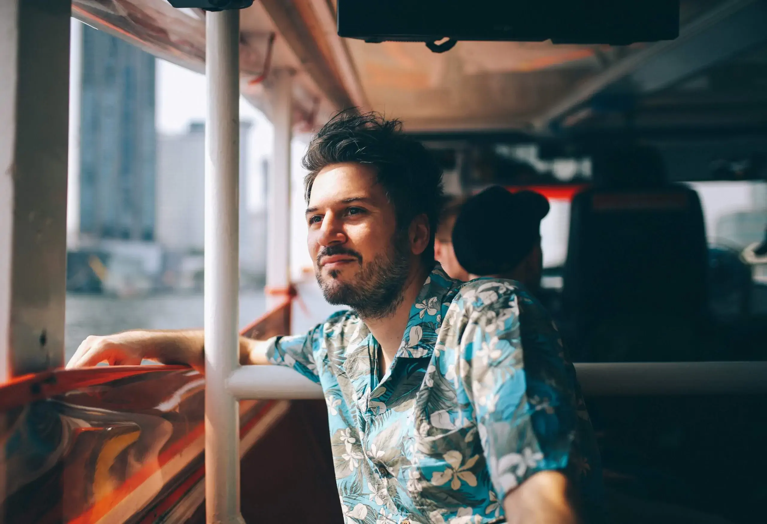 A man dressed in a blue Hawaiian shirt admiring the scenery from a ferry boat.