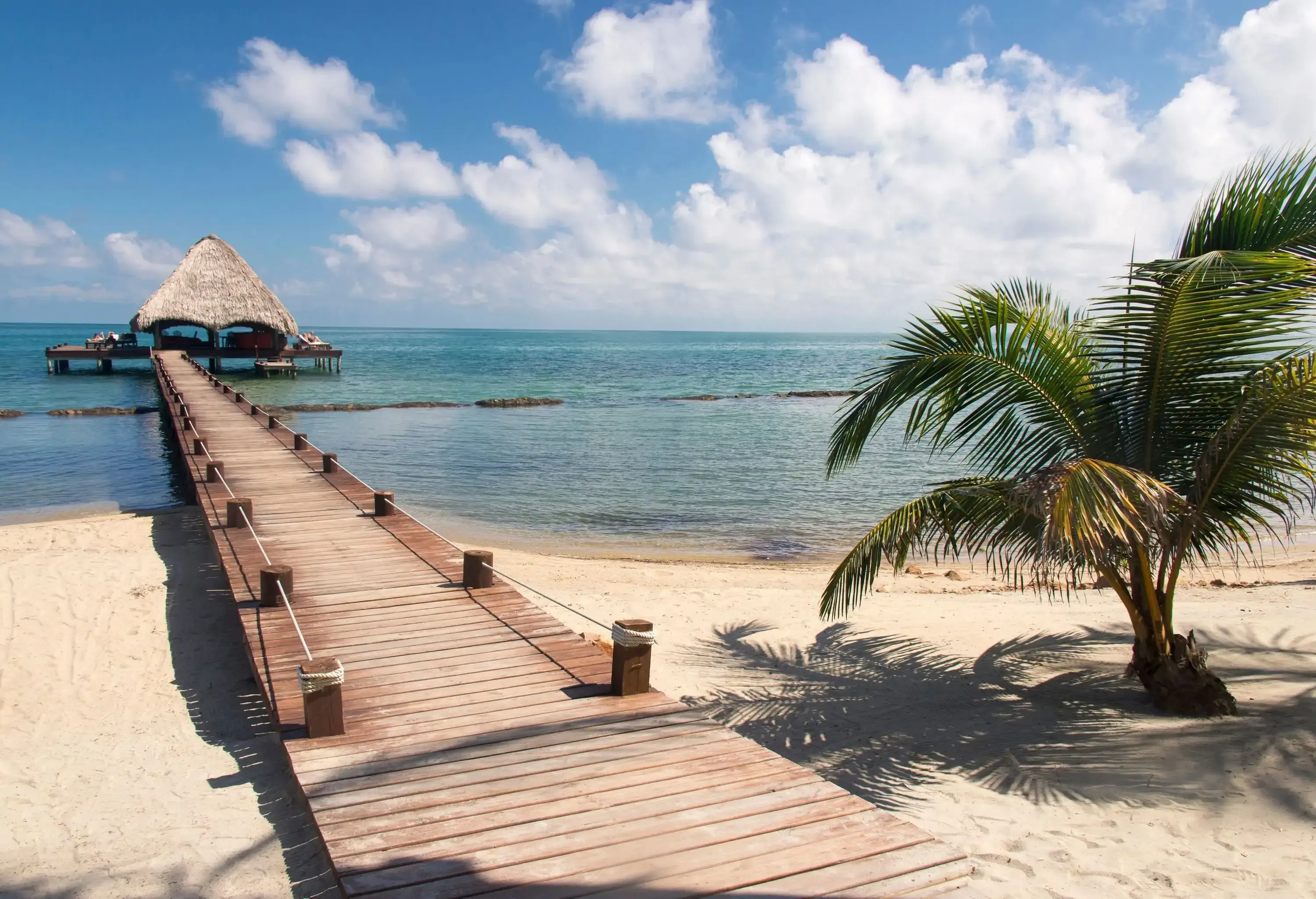 Placencia, Belize. Roberts Grove Resort, Pier leads from sand beach to thatch roof dock used as entertainment bar at night