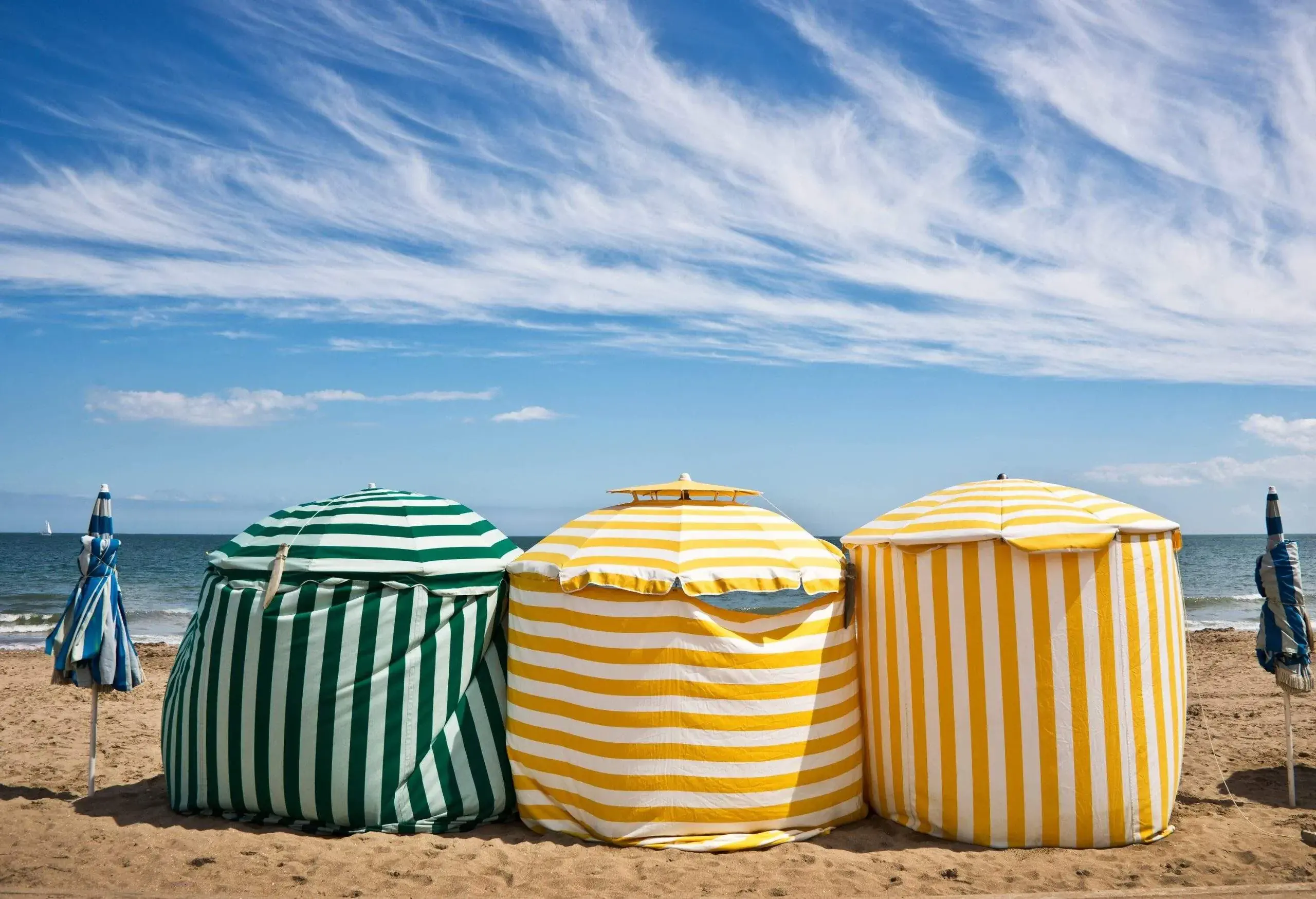 Colourful striped tents standing on golden sand along the shore.