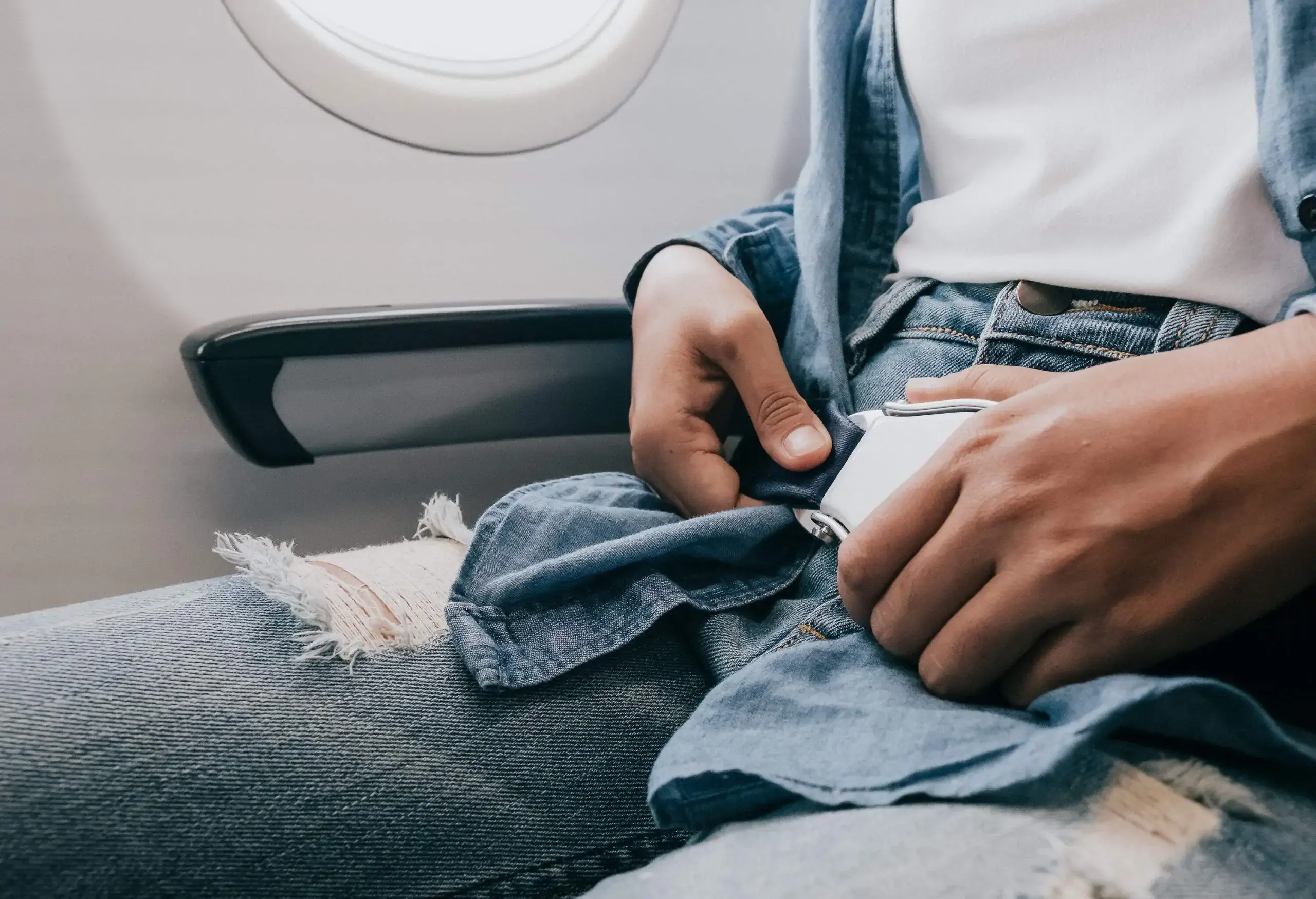 A woman fastens his seatbelt while seated inside an airplane.